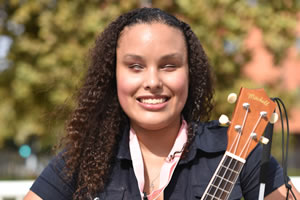 Precious Perez, Vice President. A latina with curly black hair holding a ukulele and smiling.