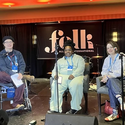three people, one black, two white, one in a wheel chair sitting in a work studio with the words and logo for Folk behind them on the wall.