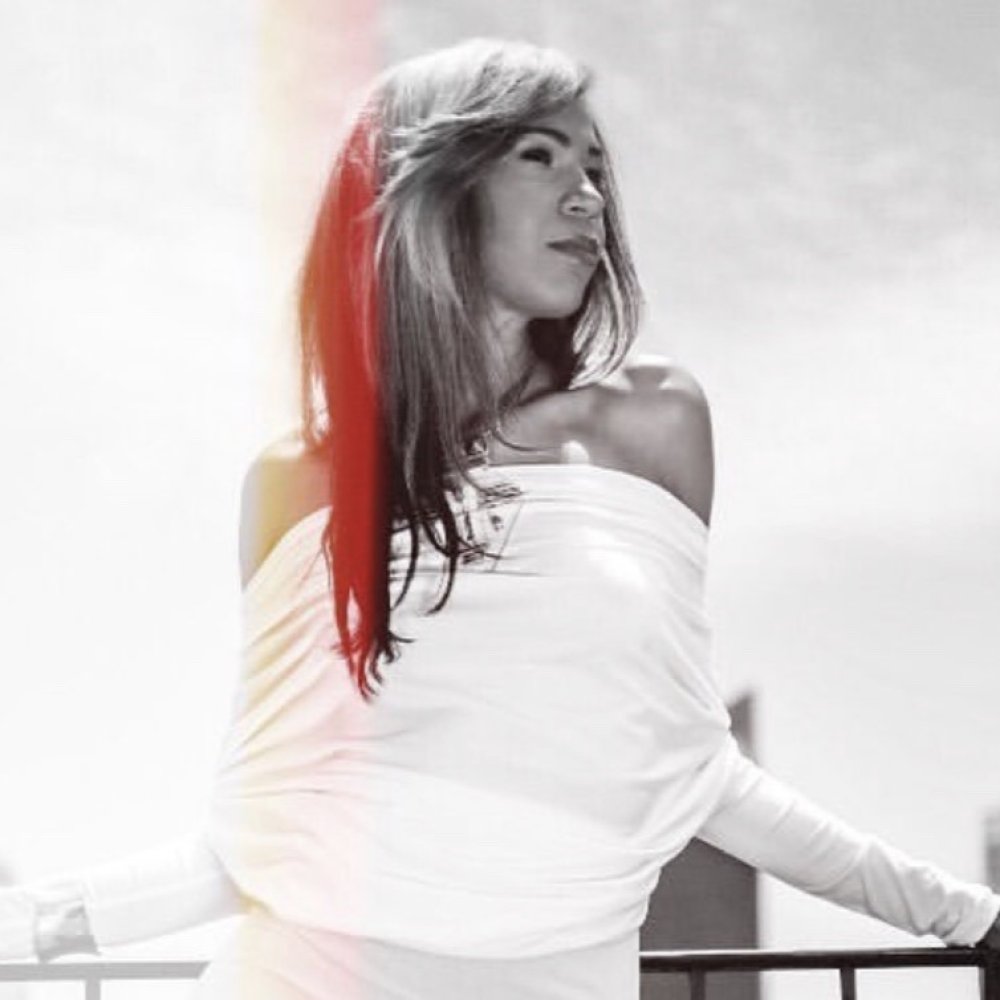 This image shows a woman standing confidently outdoors, dressed in an elegant white off-shoulder outfit, with a soft light creating a calm and serene atmosphere.