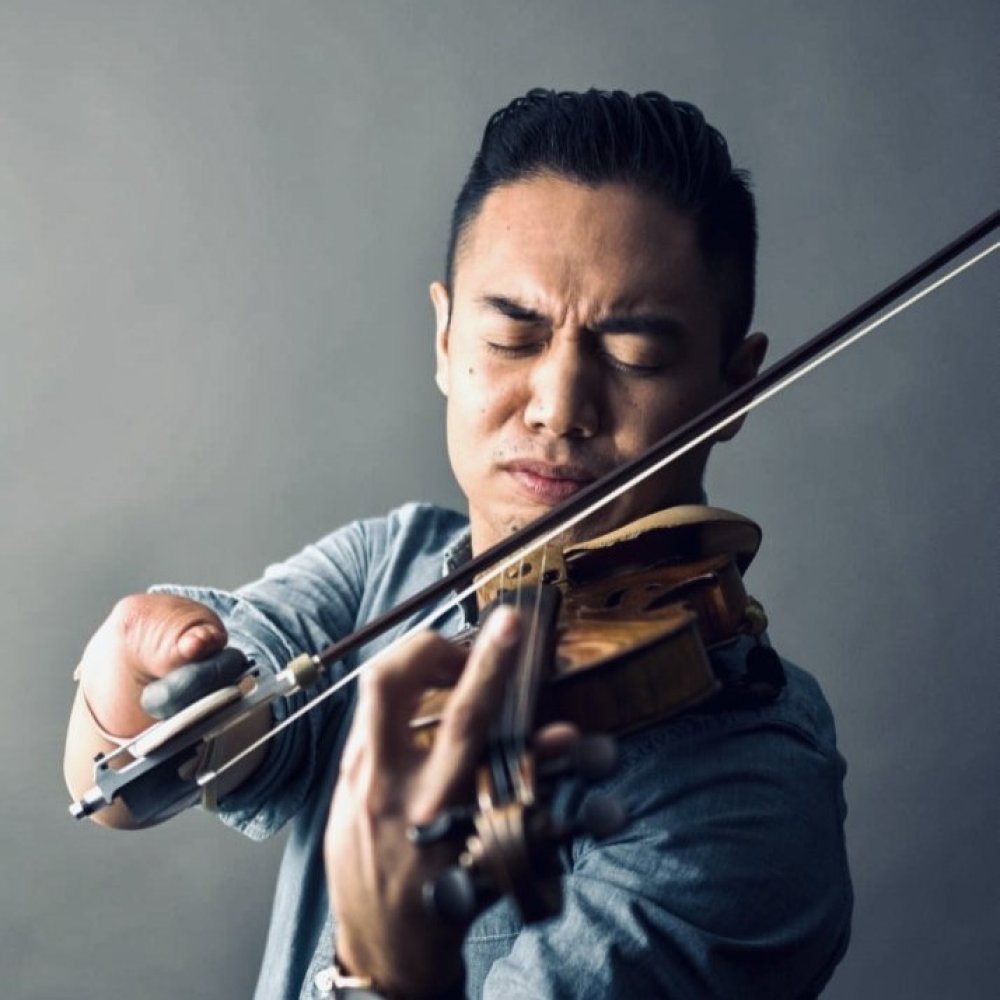Person with violin resting on shoulder while focusing on playing the instrument intensely