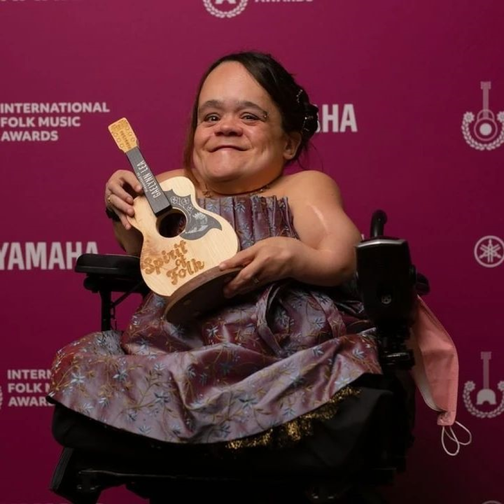 Gaelynn Lea sits with an award shaped like a ukulele