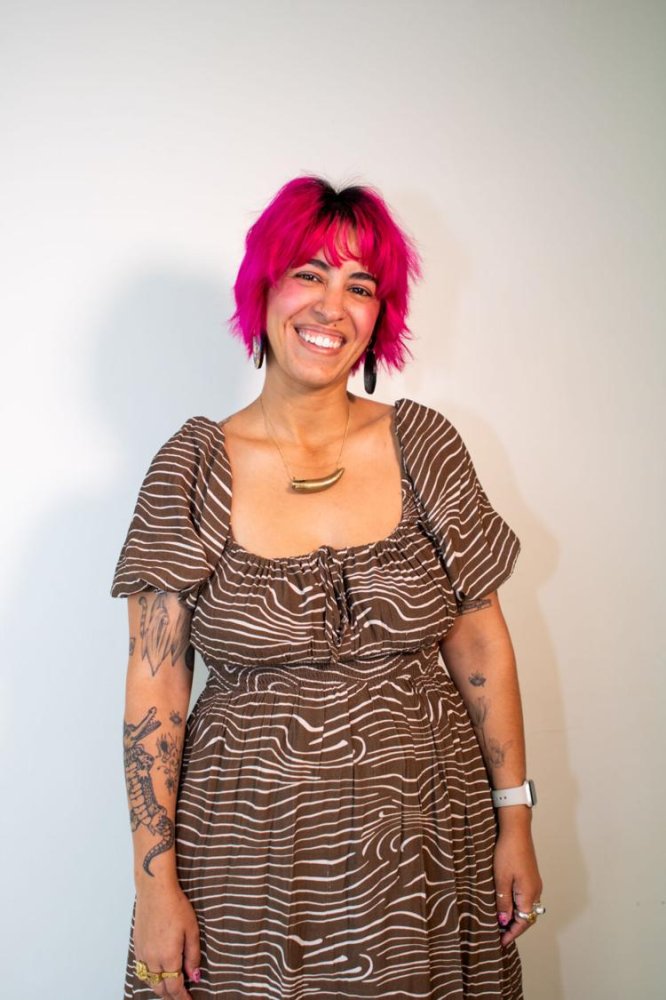 A person with pink mid length hair, brown skin, and a brown dress on.